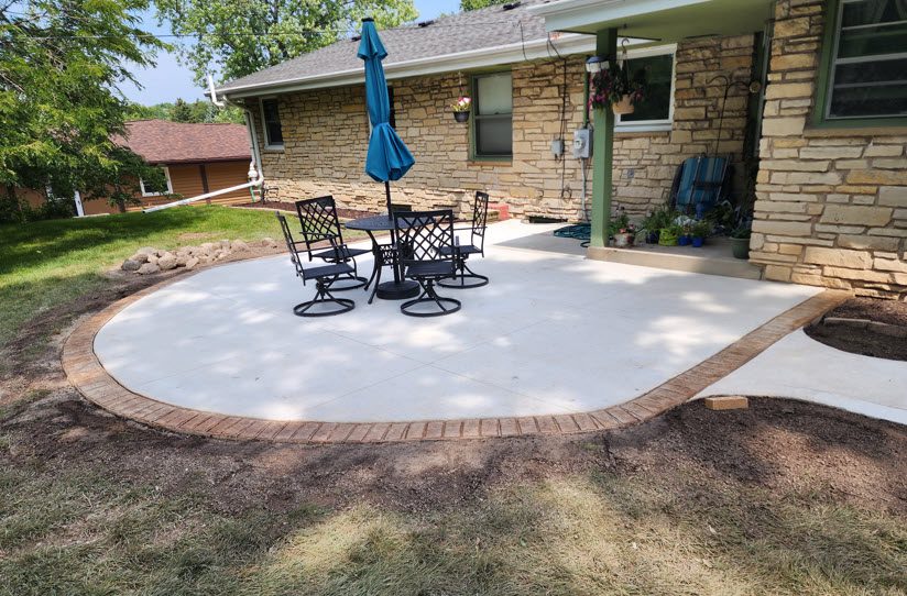 Concrete patio with black metal chairs and a blue umbrella, showcasing expert installation by Morici Bros Concrete LLC, designed for outdoor relaxation and enhancing home value.