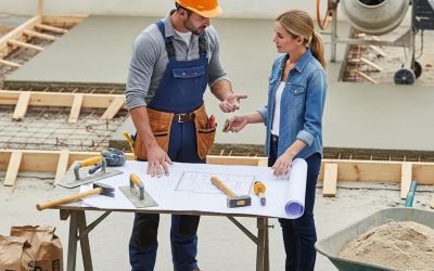 Concrete contractor discussing project plans with homeowner at a construction site, showcasing blueprints and tools.