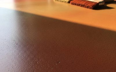 Stained concrete surface showcasing rich earthy tones and texture, with a paintbrush, relevant to durable concrete garage floors and aesthetic enhancements in West Allis, WI.